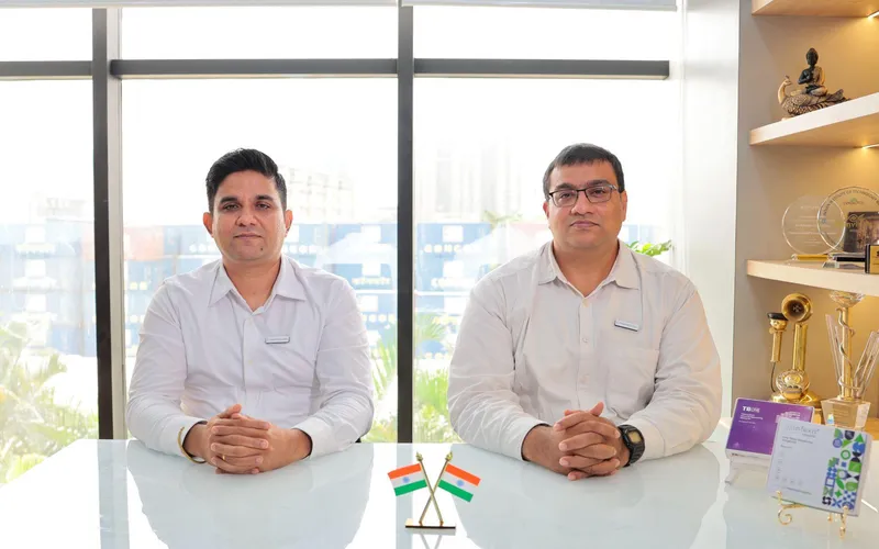 HaystackAnalytics co-founders seated at their office desk, with crossed Indian flags on the table and awards on the shelf behind them